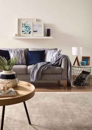 Grey textured sofa with deep blue and striped cushions, neutral rug and round coffee table