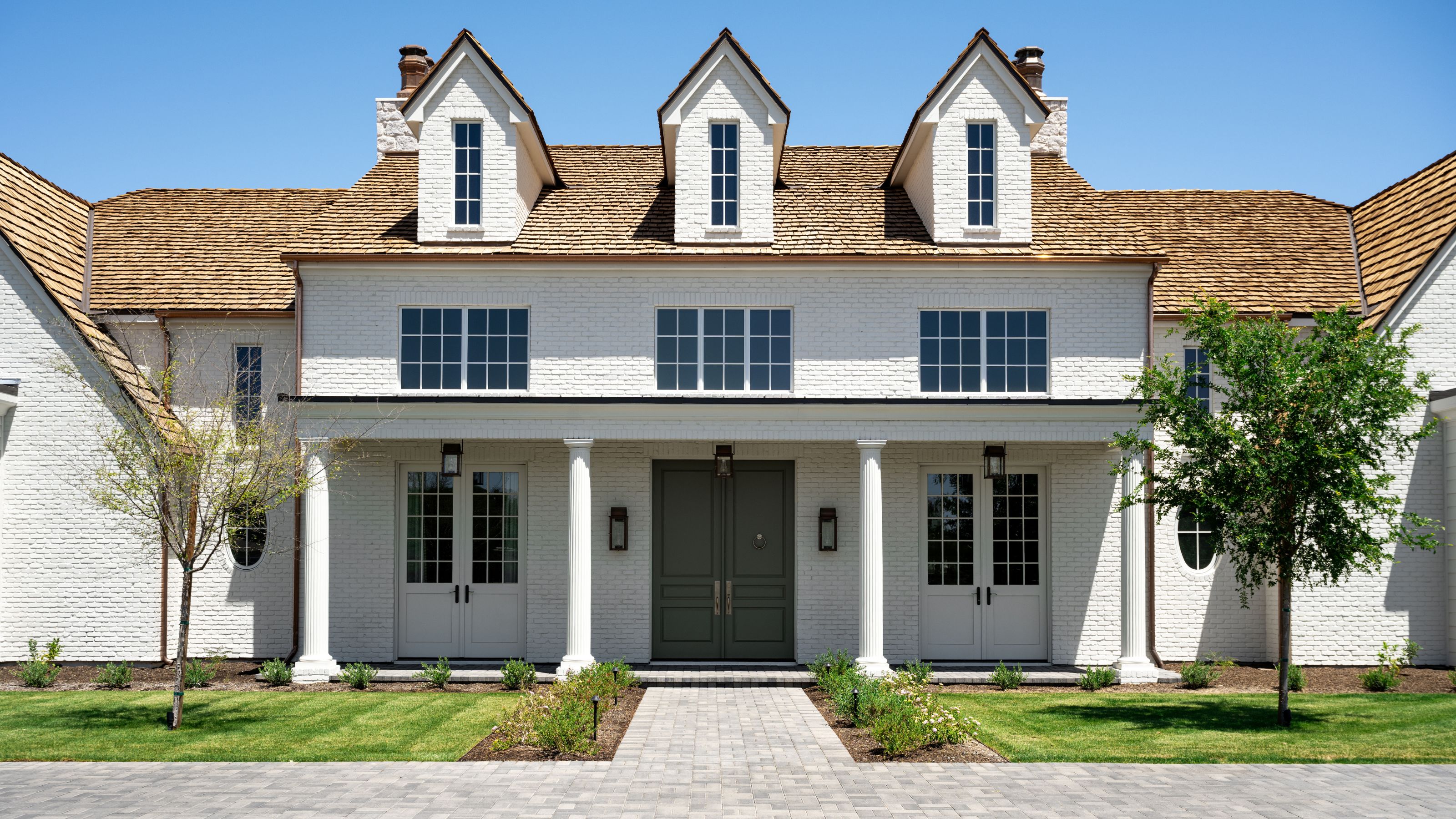a large white rendered home in Arizona with pillars, a green front door and front lawn with small trees