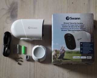 a box with a white security camera and all of its contents laid out on a wooden surface