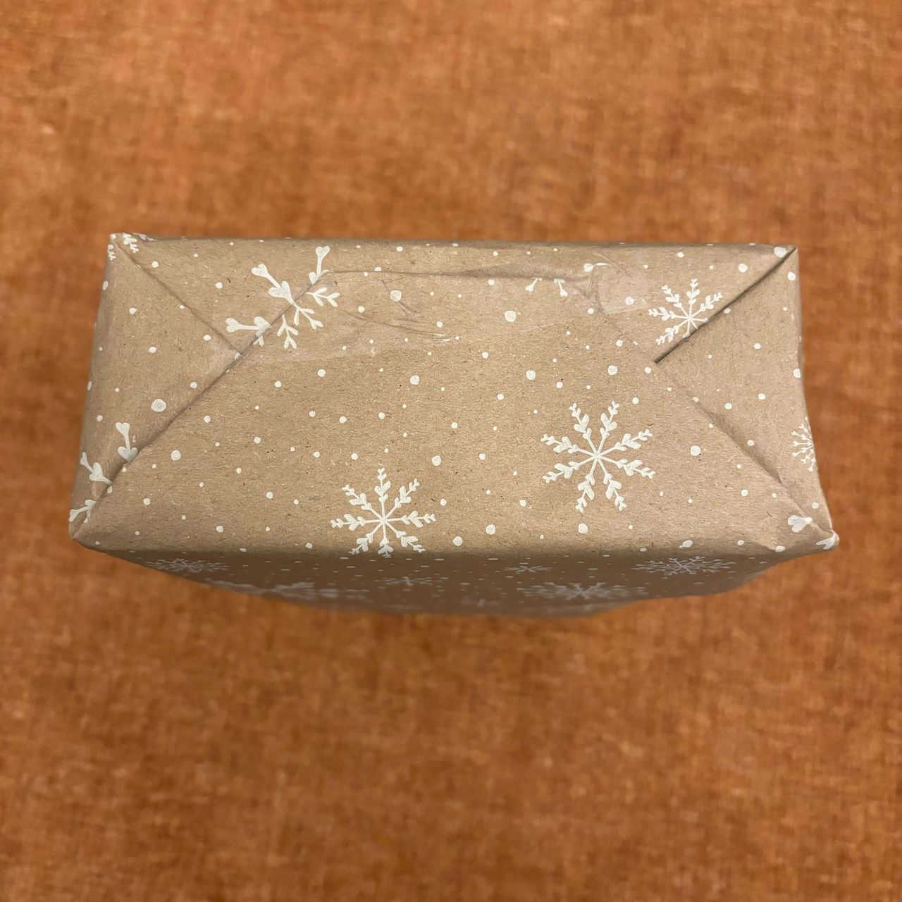 A rectangular box wrapped in brown paper with a white snowflake print on it