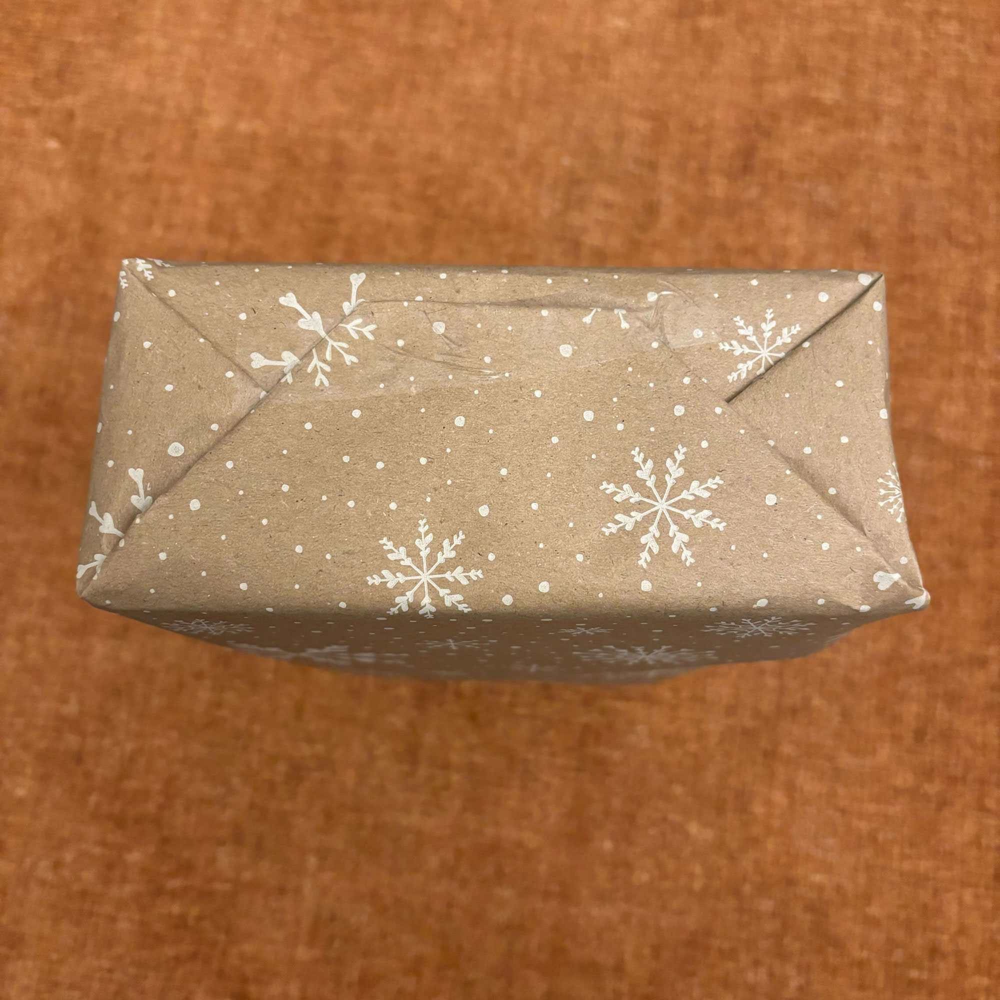 A rectangular box wrapped in brown paper with a white snowflake print on it