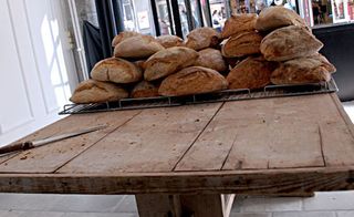 A wooden table with loaves of bread stacked on a metal tray.