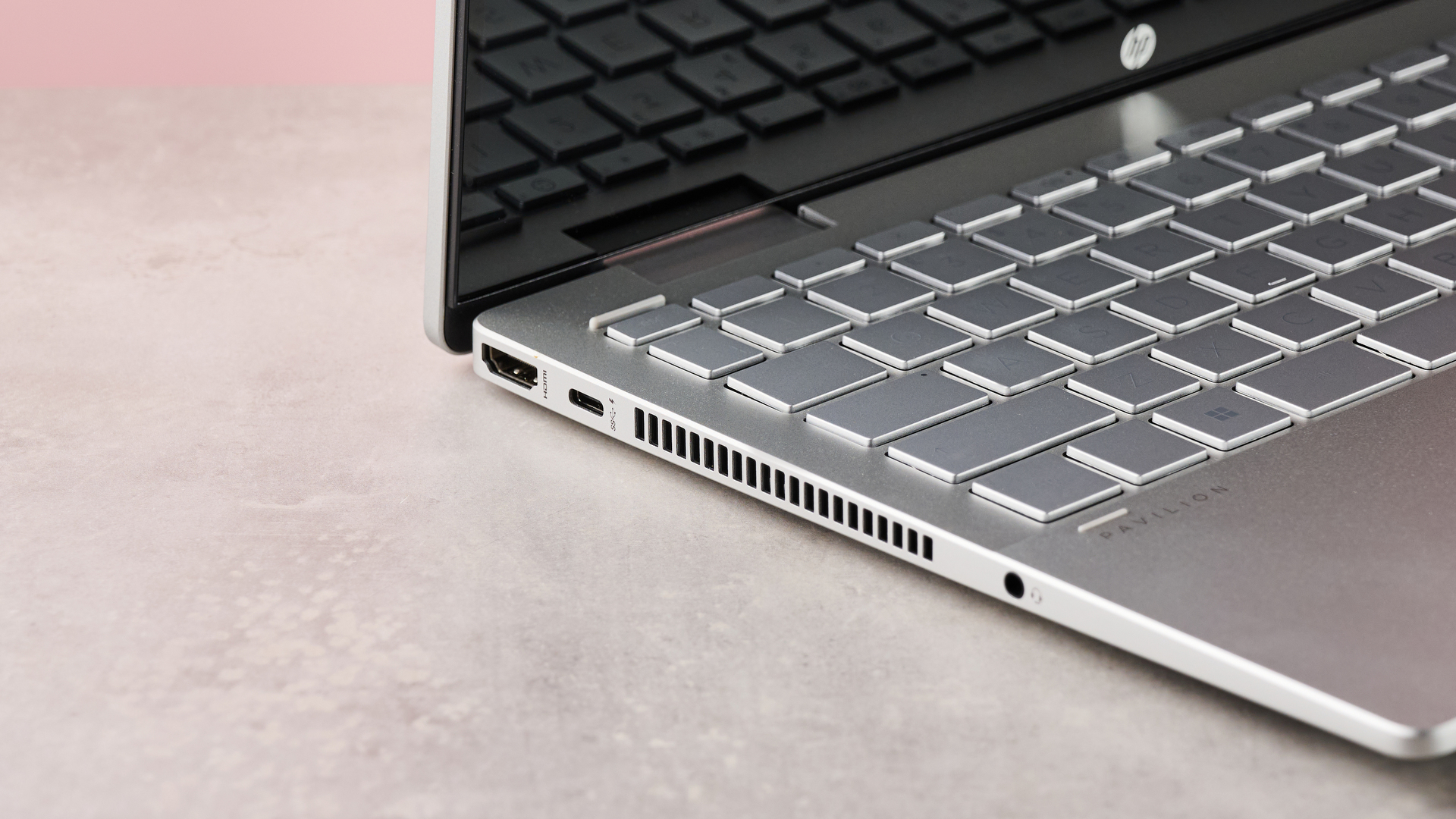 Close-up of left-side ports on HP Pavilion x360 14, with desk and pink wall in background