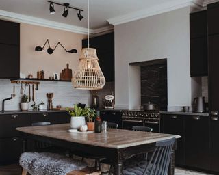 A black kitchen with rattan pendant ceiling light, wooden dining table and faux fur throw on seat