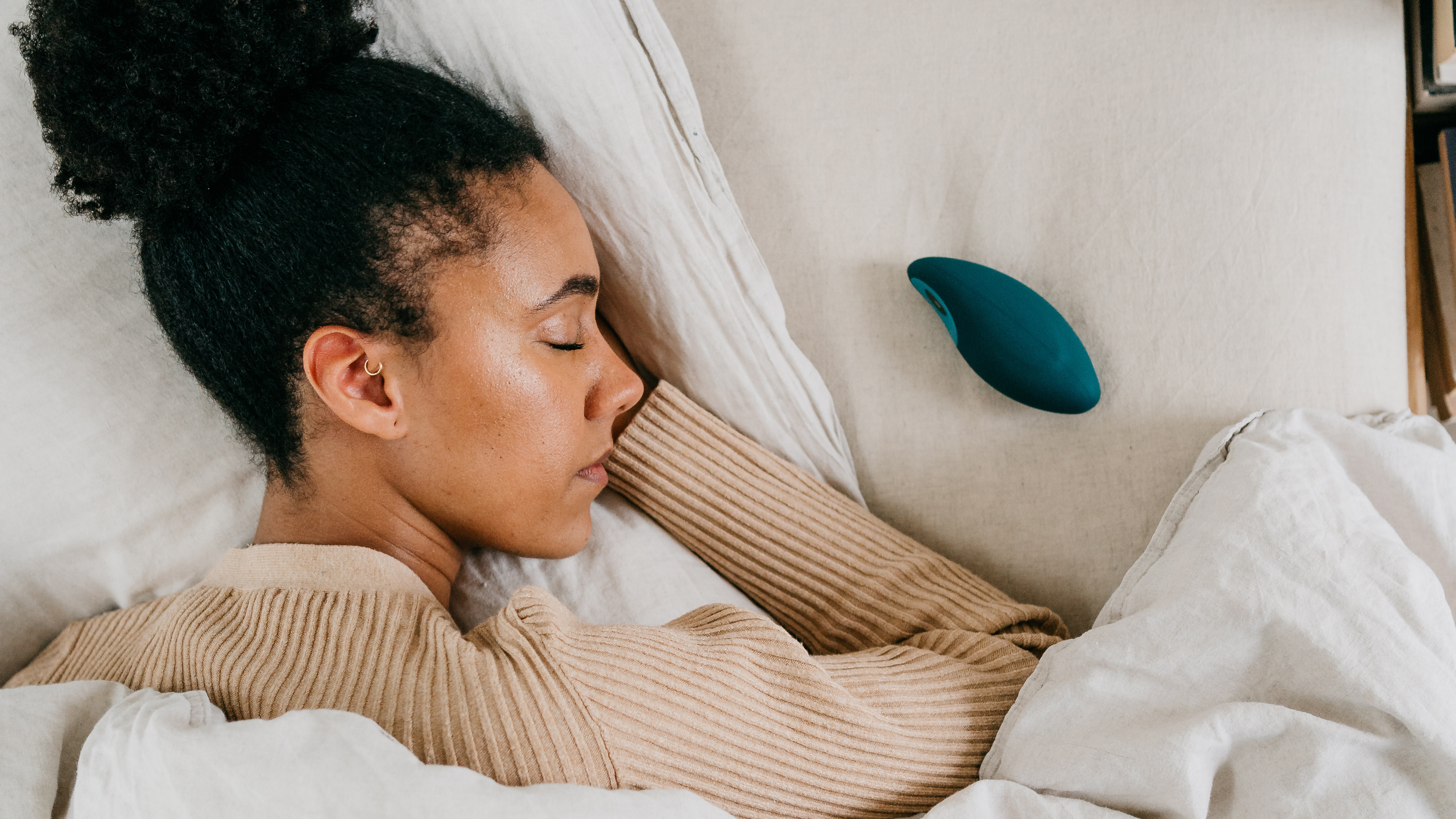 A woman sleeps peacefully in bed after using the moonbird device for reducing insomnia, stress and anxiety. A blue moonbird sits on the bed next to her pillow