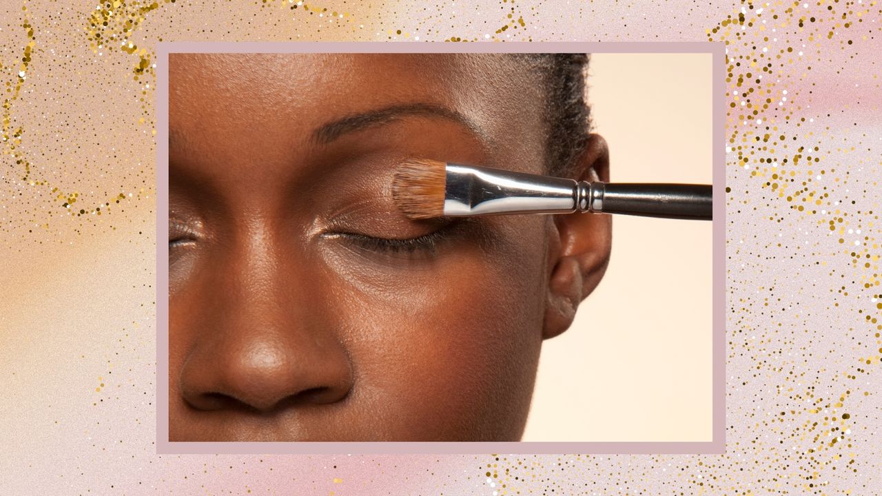 A close up of a woman&#039;s left eye, with a brush applying a shimmery eyeshadow to her lid/ in a pink and yellow gradient template with a gold glitter overlay