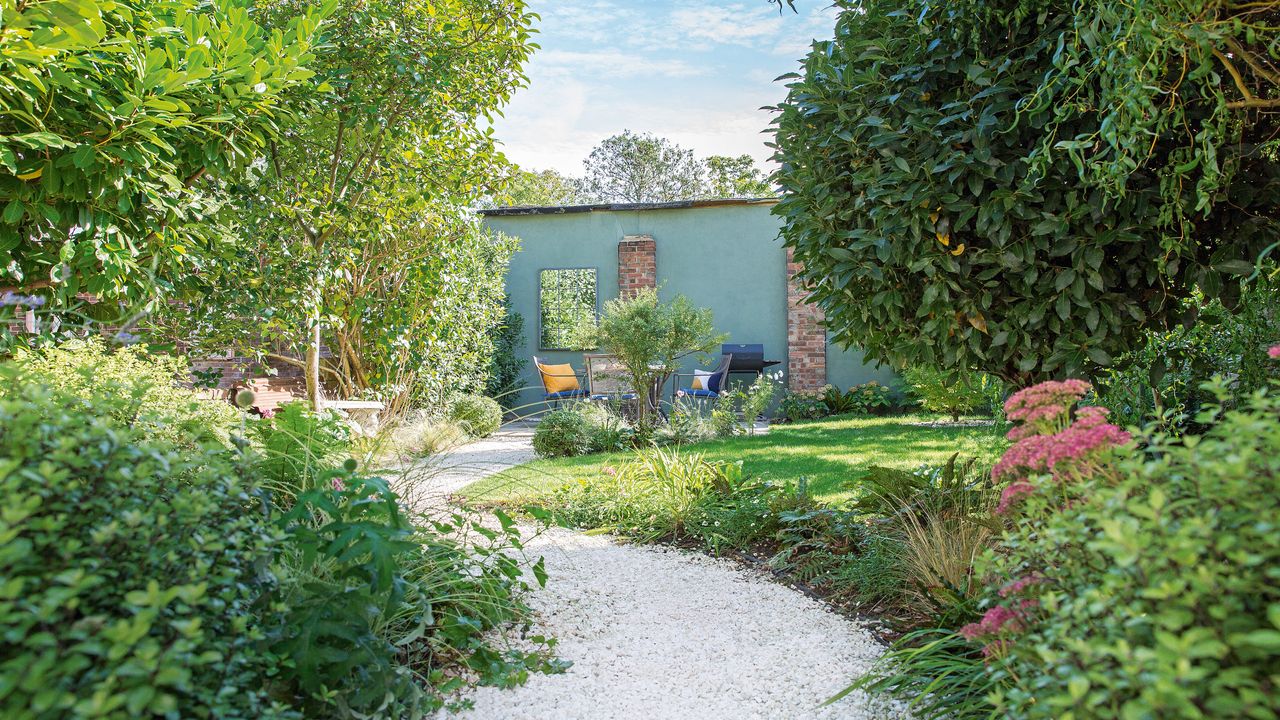 gravel path winding through the garden with lawn and flowerbeds to a seated area between trees 