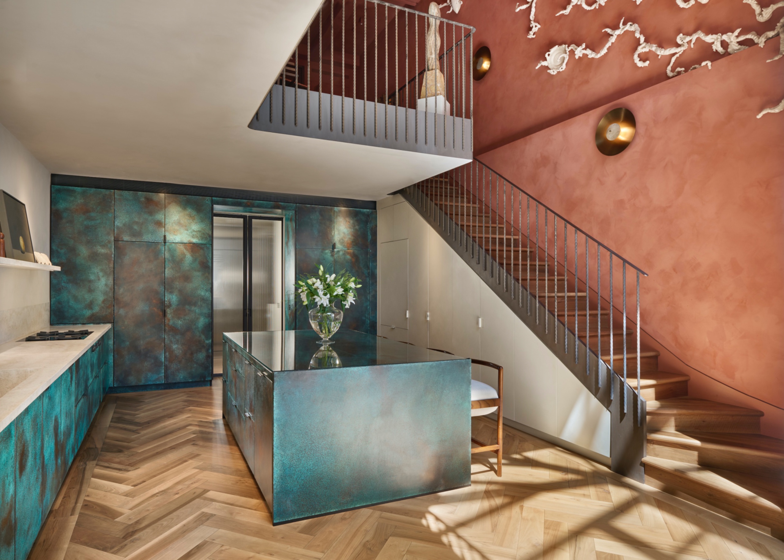 Verdigris copper kitchen cabinetry in shifting sea-green and turquoise tones, paired with terracotta plaster walls and timber flooring.