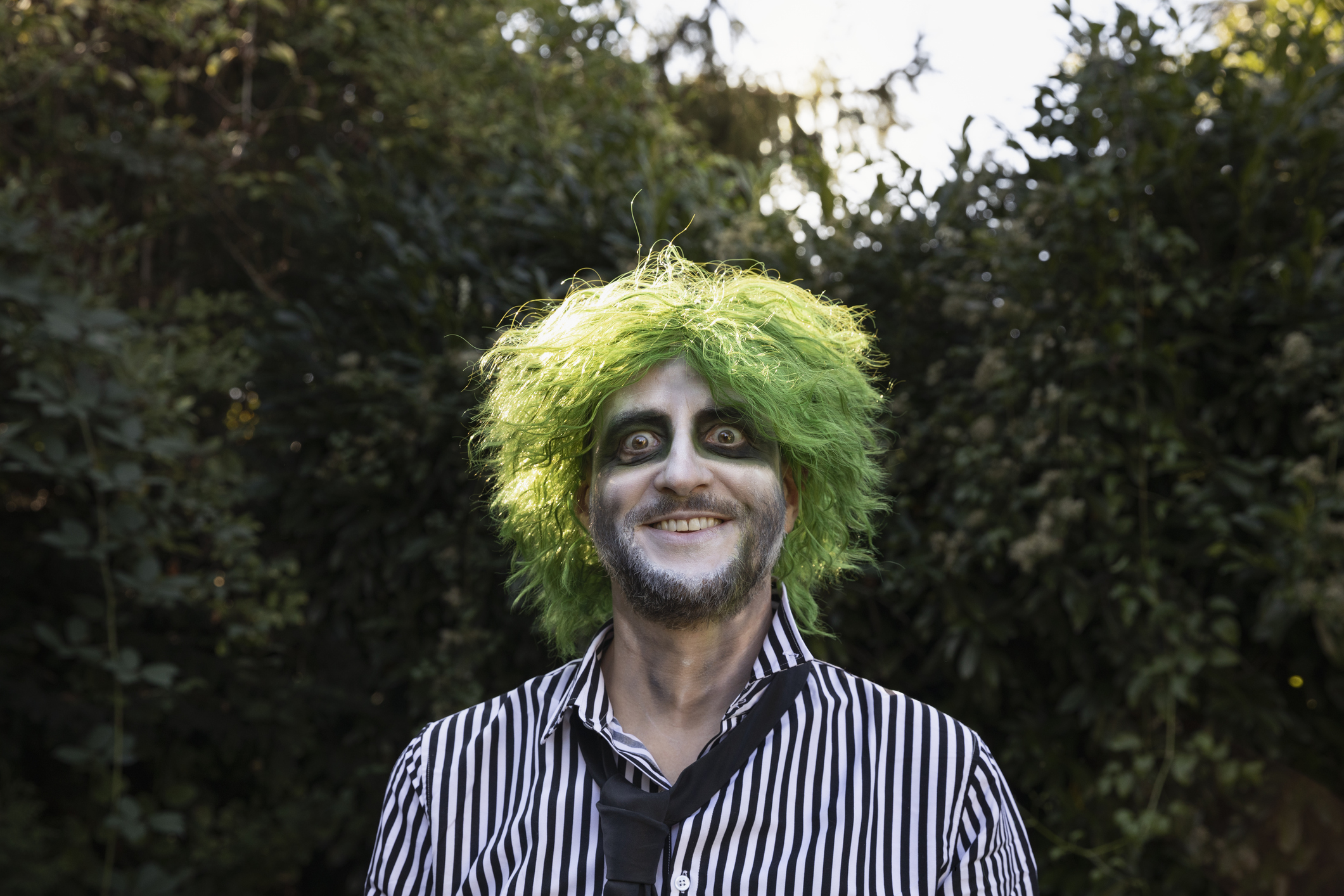 Mature adult wearing a shirt and tie, with green wavy hair, Halloween face paints and carefree facial expression