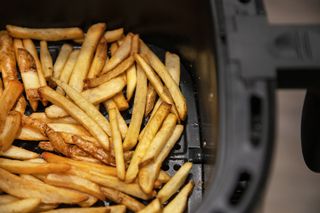 A portion of freshly cooked golden chips in the tray of an air fryer.