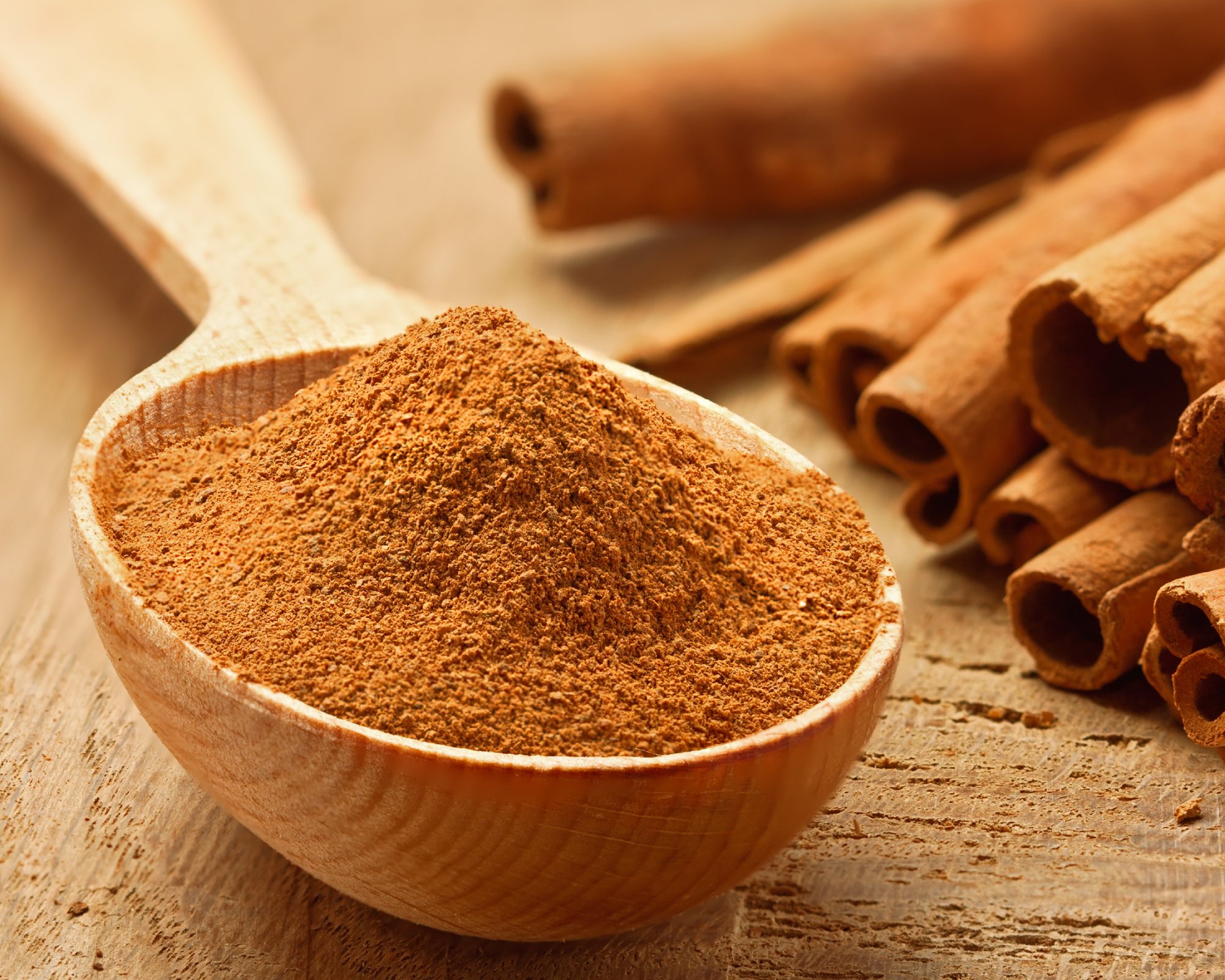 scoop of powdered cinnamon with cinnamon sticks in the background
