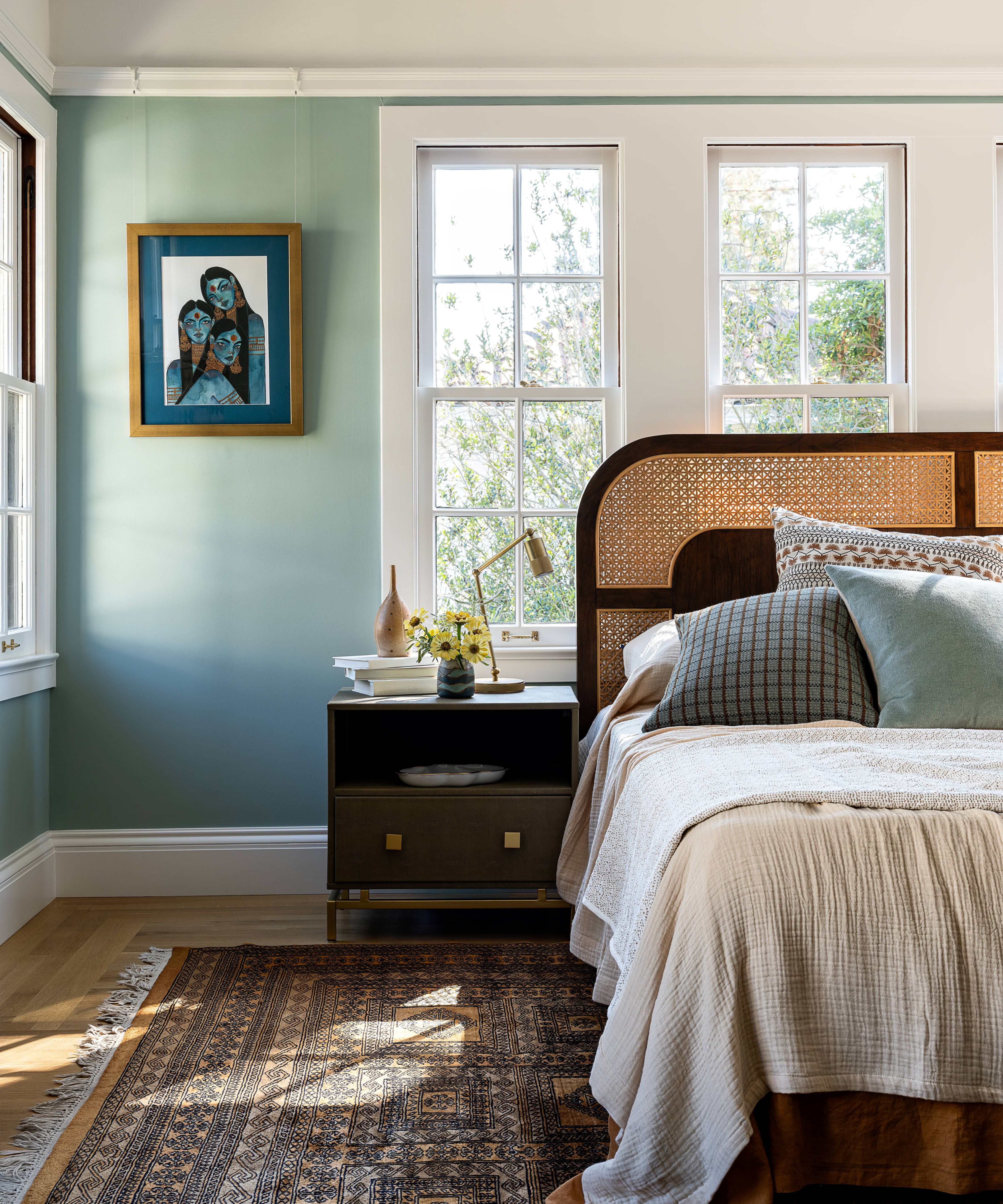 a bright bedroom painted blue with lots of windows and a wooden rattan bed