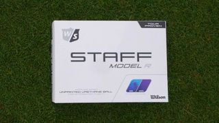 Wilson Staff Model R Ball and its white packaging laid down on the green