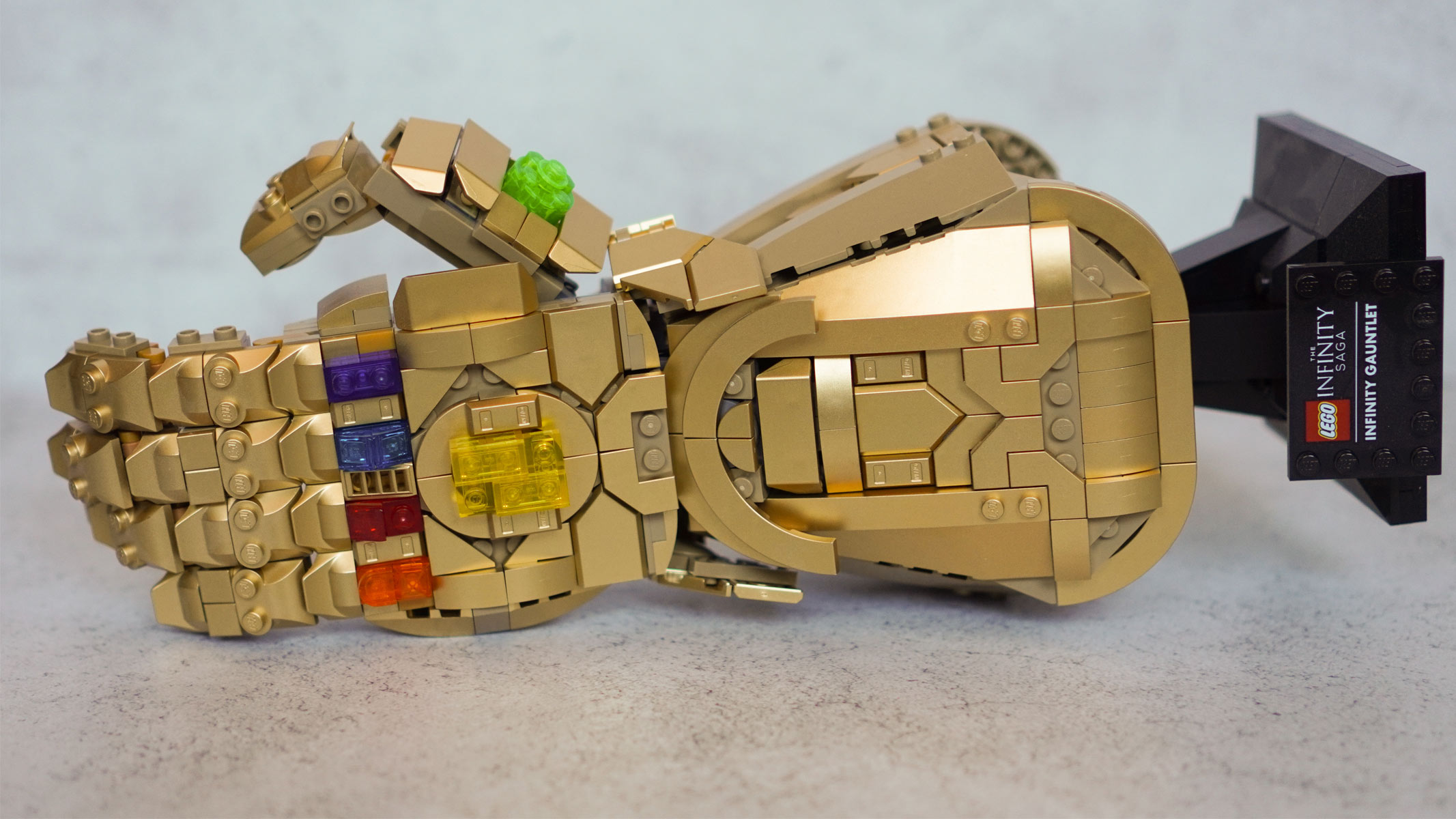 A bust of a hand and wrist is made from gold bricks and features a display stand and multi-colored stones on the back is laying on its side on a grey background.