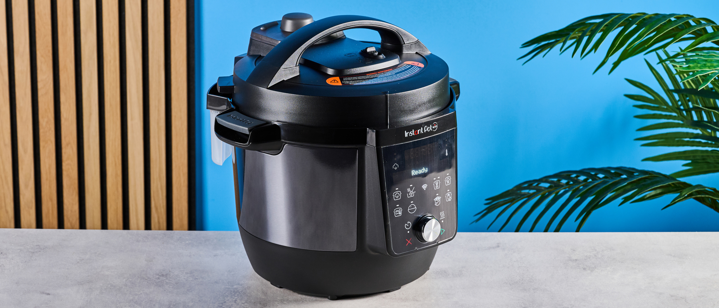 Instant Pot Plus photographed in front of a blue background. 