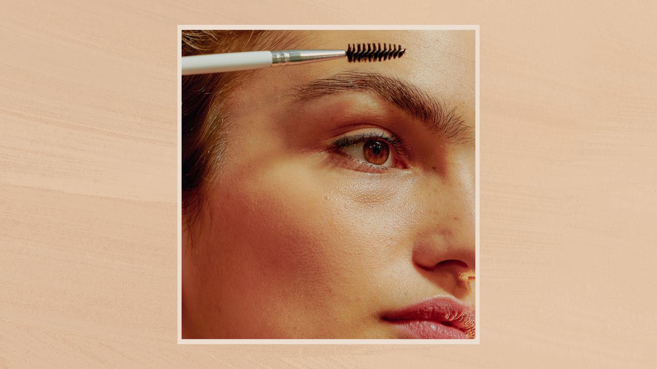 Image showing close up of woman using her spoolie to brush her eyebrows, in a cream frame against a beige watercolour-style background