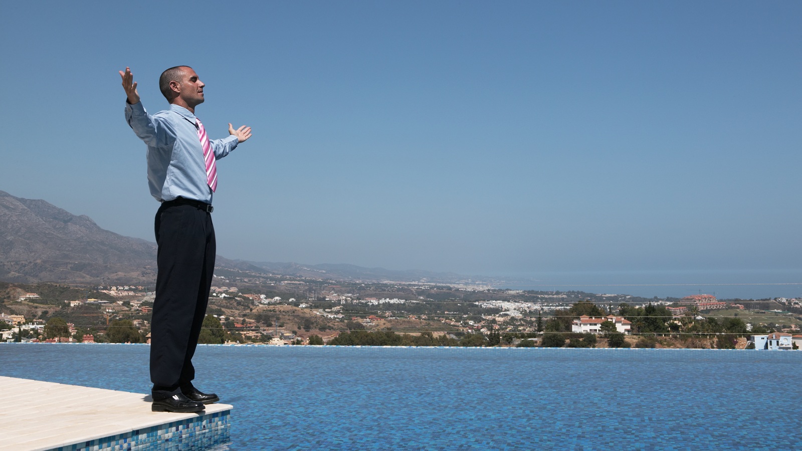 A businessman stands at the edge of a pool.
