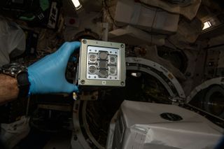 an astronaut on the space station holds a metal cube with eight apertures on it