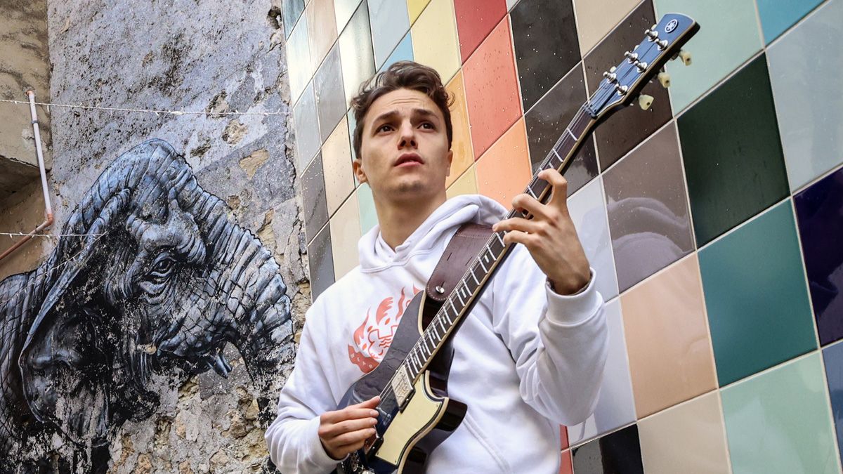 Matteo Mancuso holds a Yamaha guitar in front of a mural