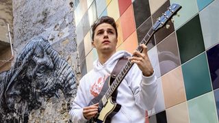 Matteo Mancuso holds a Yamaha guitar in front of a mural