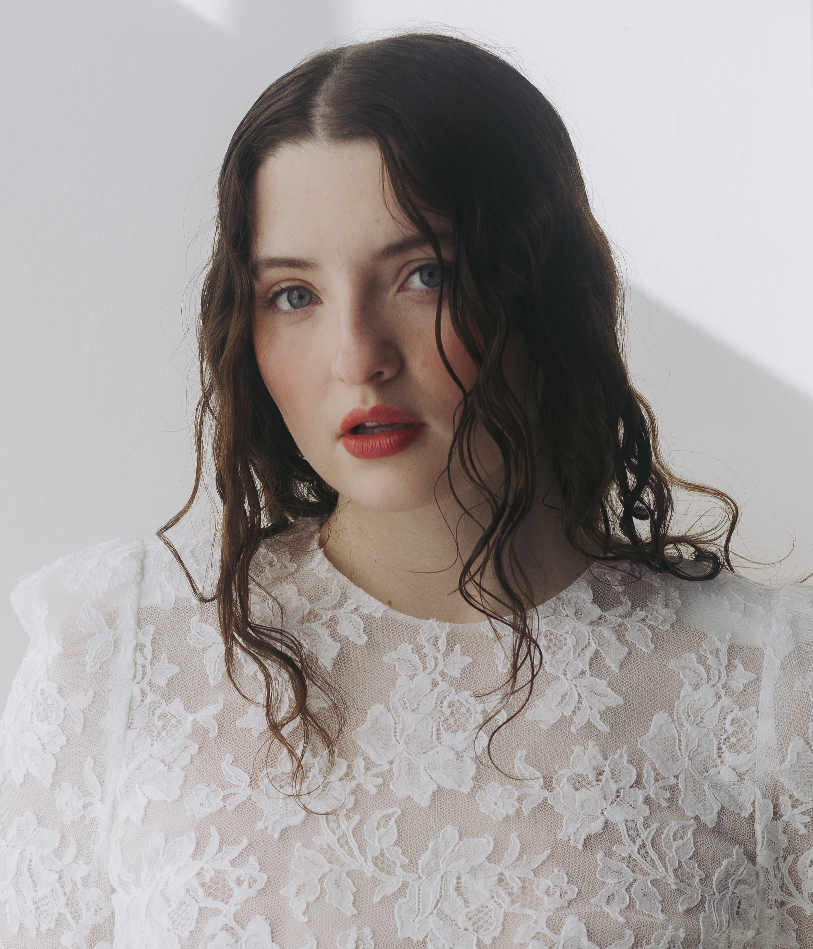 the testaments actress lucy halliday poses in a headshot wearing her hair curled and wet draped over a white lace dress