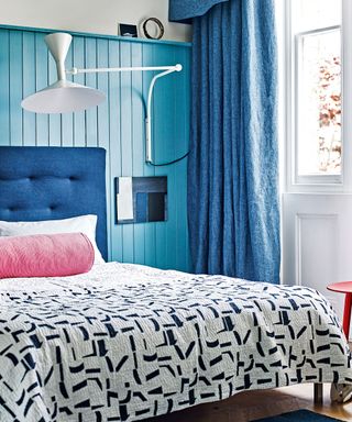 A blue pannelled wall with statement bedroom wall lighting ideas and pink and blue soft furnishings.