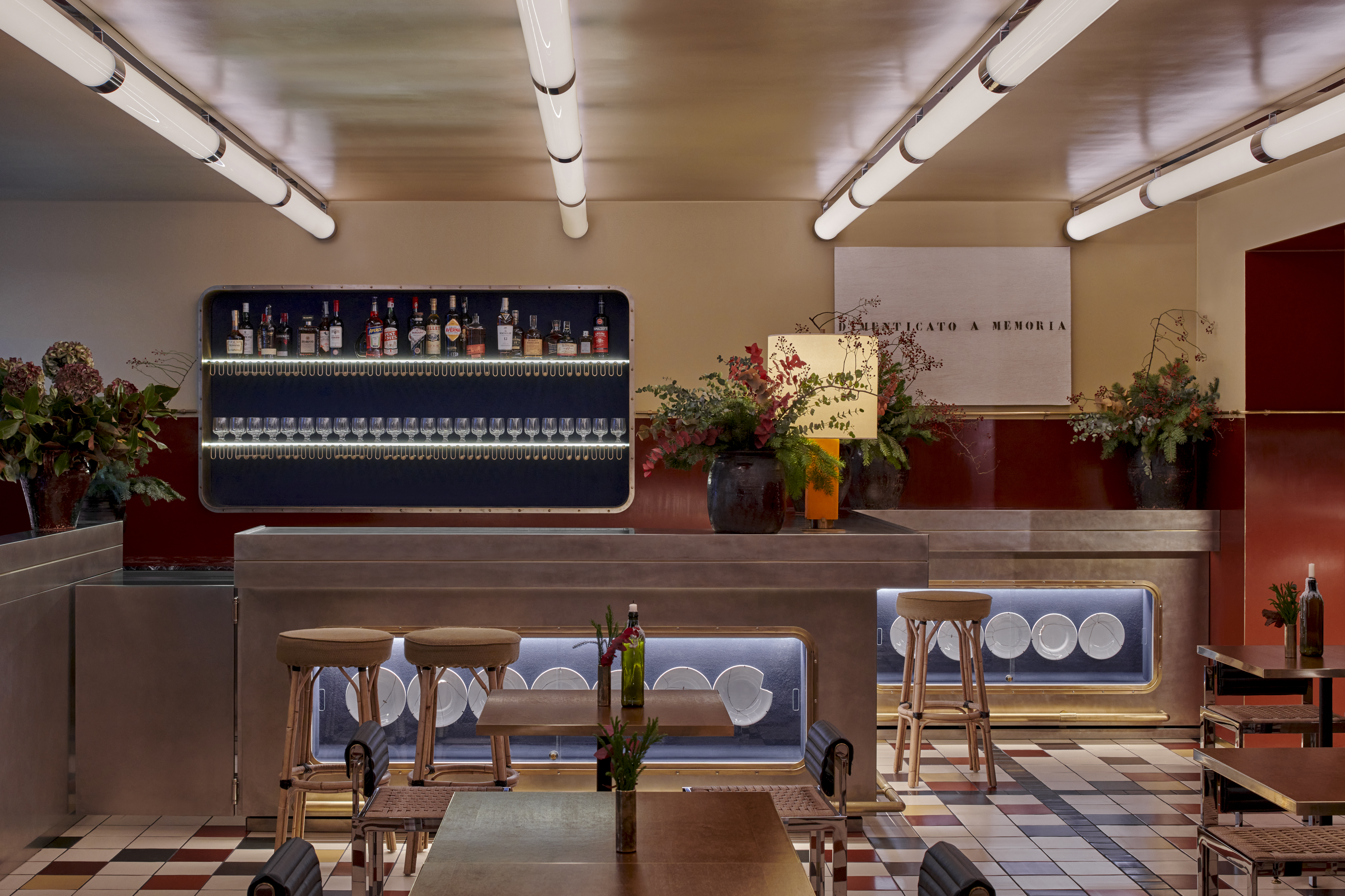 Two rooms of a restaurant, the first one dressed in brushed stainless steel, with sculptural lighting, plush velvety banquettes in sea blue, and textural delays, the other, with wall-wide neon lighting, checkered floors, and round-edged detailing.