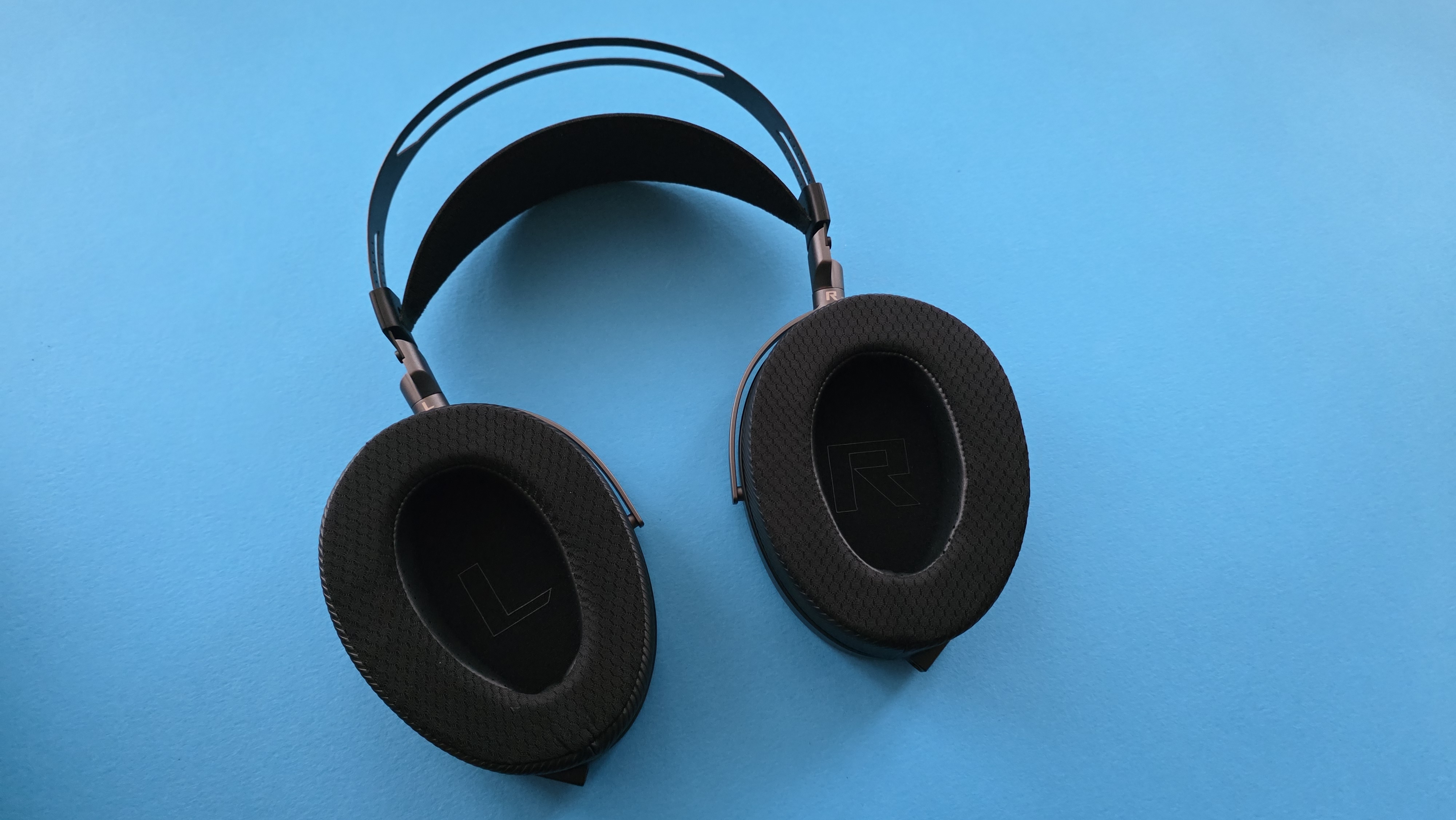 A pair of large, black, over-ear headphones with a striped grille design rests on a blue surface.