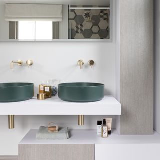 white bathroom with light brown feature panels, double green vanity sinks with gold fixings and the reflection of a patterned shower wall in the mirror