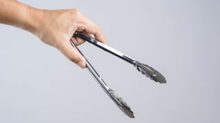 A hand holding a pair of stainless steel tongs