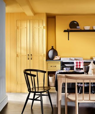 Yellow painted dining room, light wood dining table with matching dining chairs and black wooden dining chair, black flooring