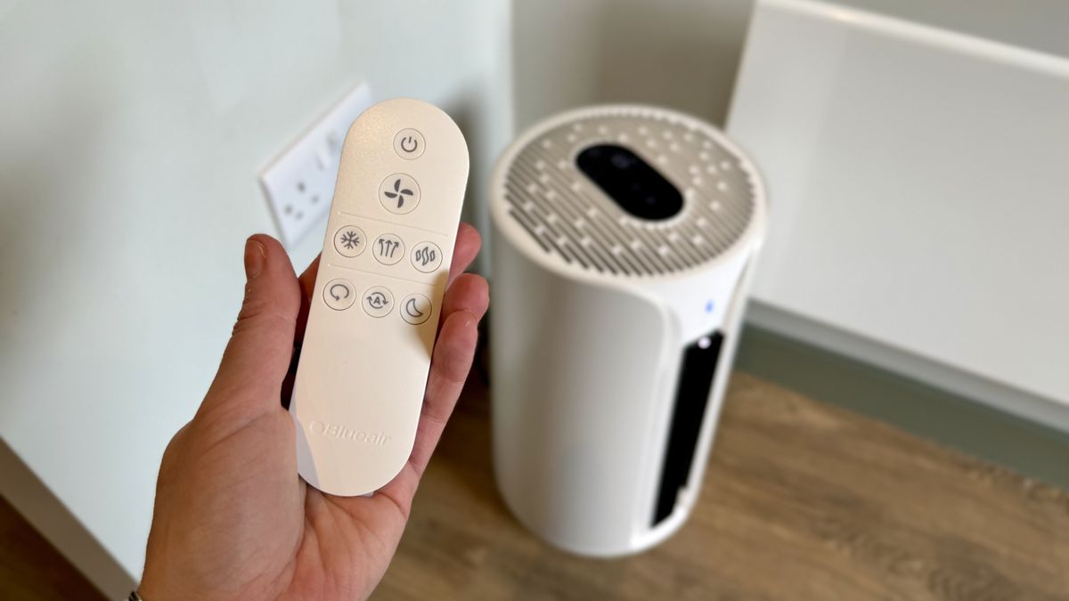 A photo of the Blueair T20i Air Purifier with its remote in a room with white walls and laminated wooden floors