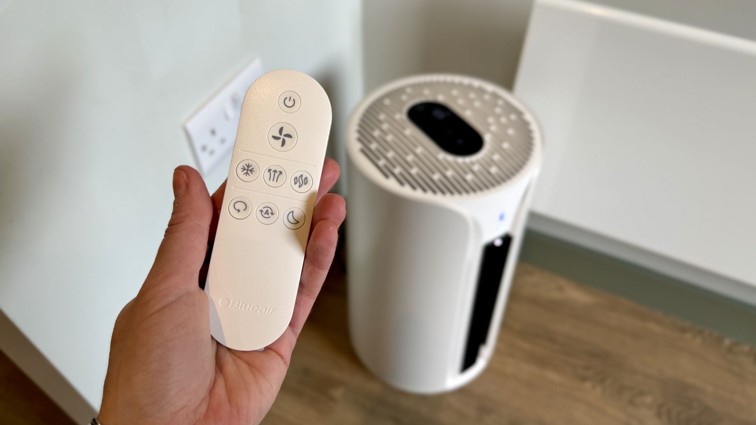A photo of the Blueair T20i Air Purifier with its remote in a room with white walls and laminated wooden floors