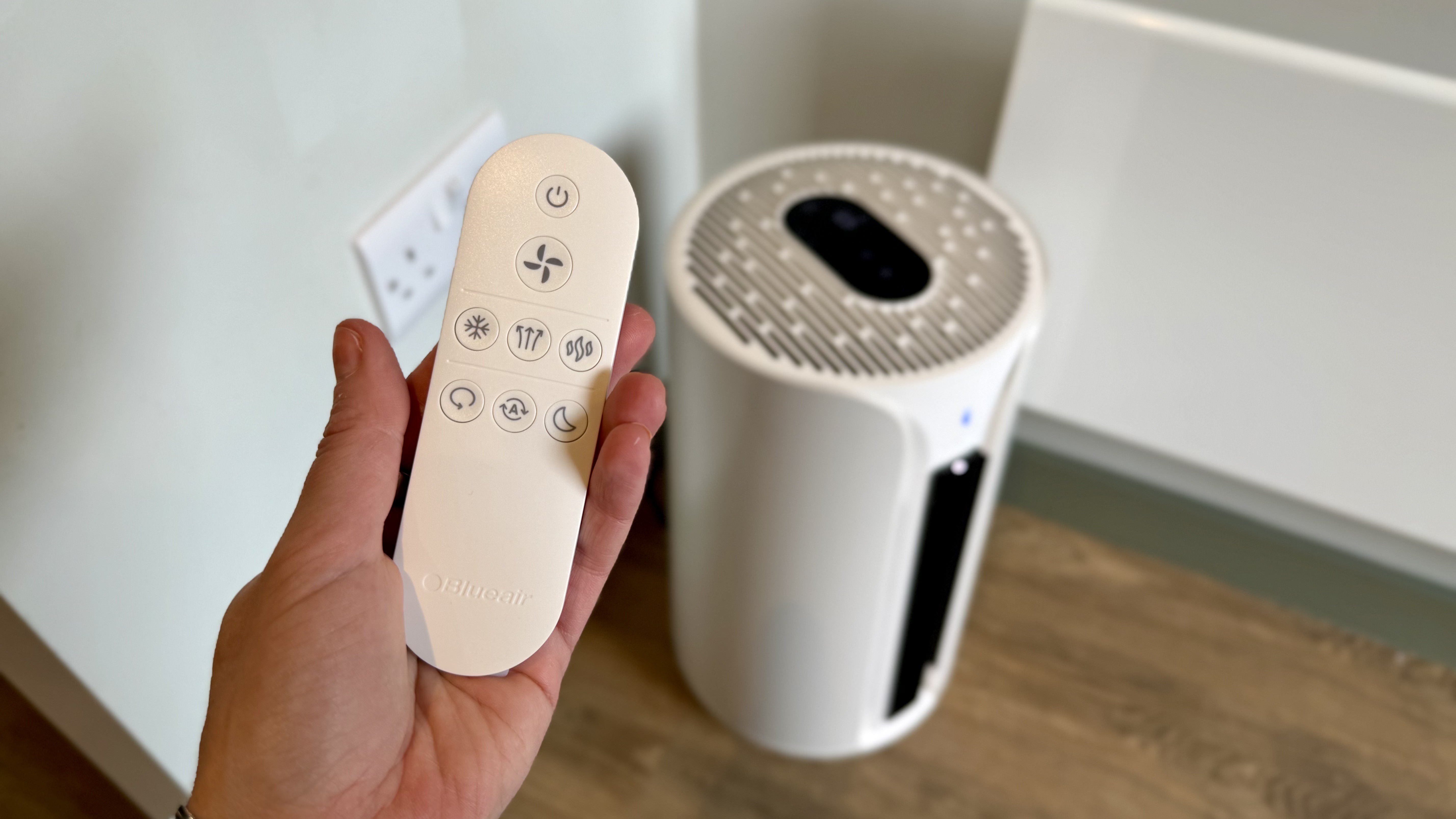 A photo of the Blueair T20i Air Purifier with its remote in a room with white walls and laminated wooden floors