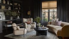 a dark charcoal color drenched snug room with curved couch, two neutral armchairs, a rug, black coffee table, and a built in bookcase and desk wall