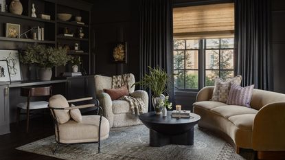 a dark charcoal color drenched snug room with curved couch, two neutral armchairs, a rug, black coffee table, and a built in bookcase and desk wall