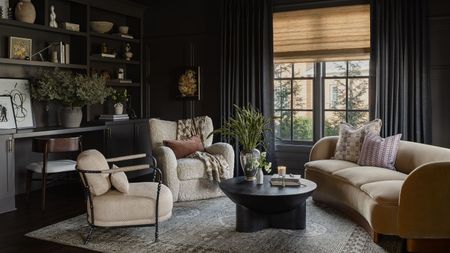 a dark charcoal color drenched snug room with curved couch, two neutral armchairs, a rug, black coffee table, and a built in bookcase and desk wall