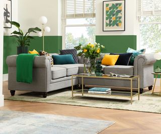 A bold living room with grey Chesterfield sofas, vibrant cushions, and green half-painted walls. Brass accents and geometric art add a fresh, modern touch.