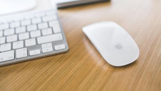 A Magic Mouse on a desk next to a Magic Keyboard.