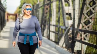 Woman looks happy as she walks along a bridge wearing earphones