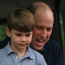 Prince William sits behind son Prince Louis and seems to be shouting while Louis looks more pensive and wears a blue and white striped polo shirt