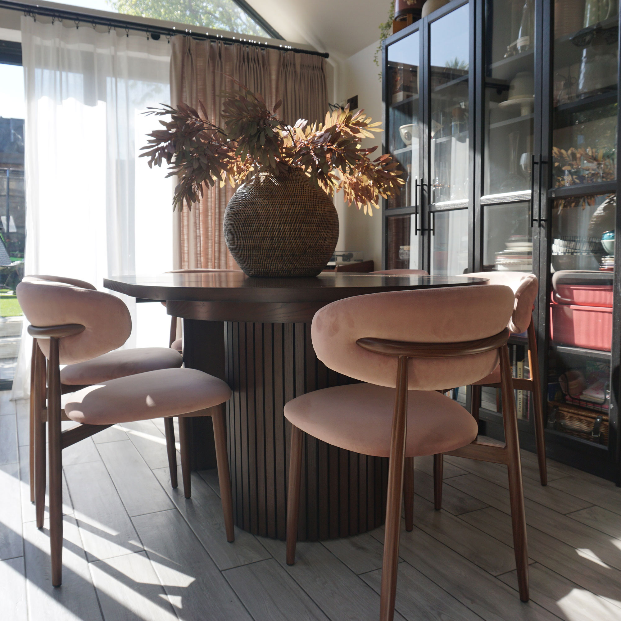 round wooden dining table surrounded by light pink upholstered chairs