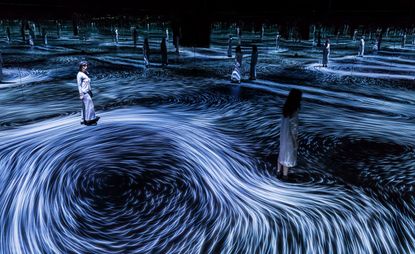 A dark exhibition space with white swirl lines on the floor and people standing. 