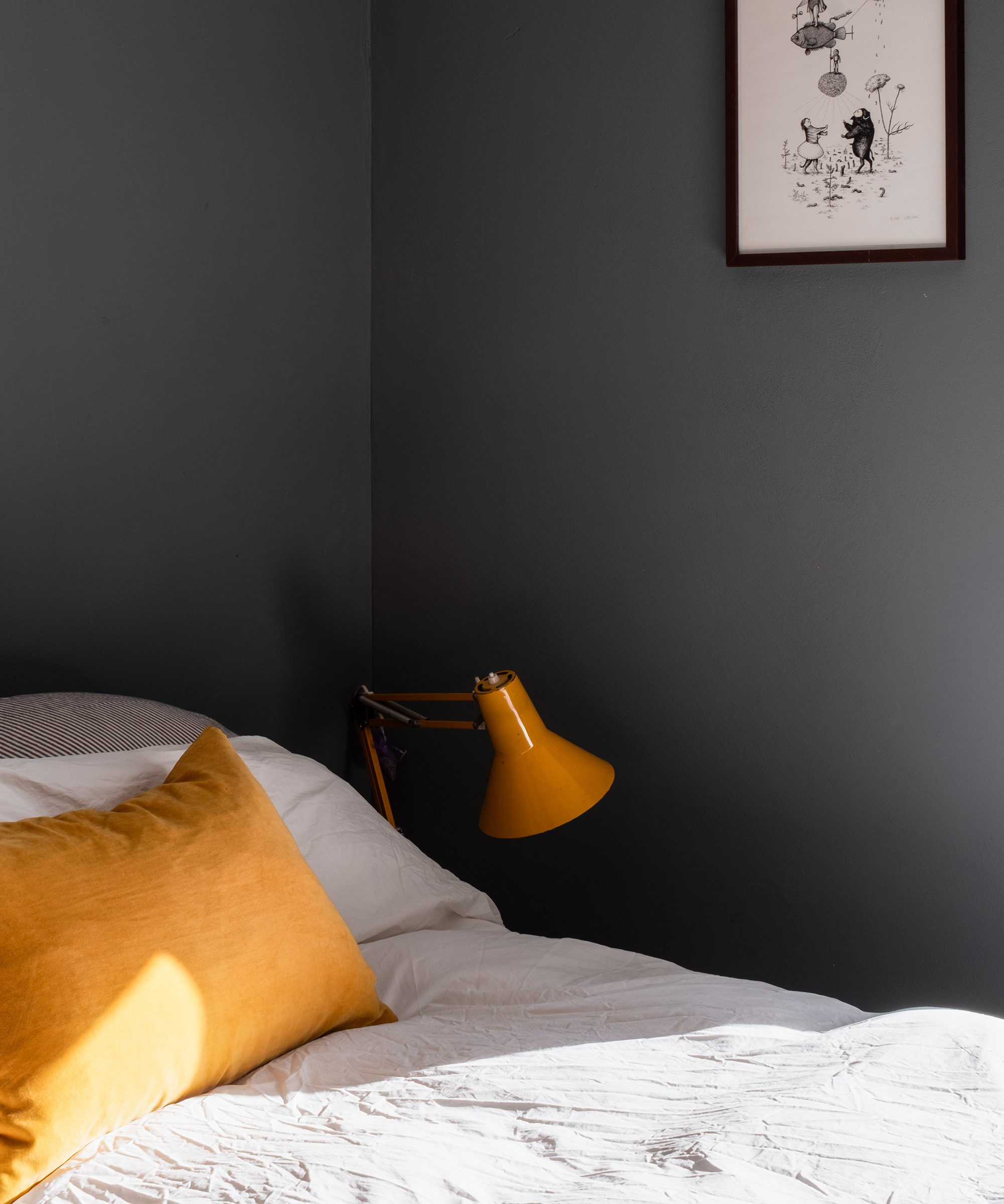 Grey walls in a bedroom with yellow cushion and bedside lamp