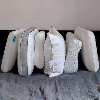 The best pillows for side sleepers being tested on a bed with a black headboard and grey bedding