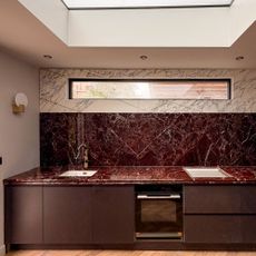 Kitchen with deep red cabinetry and deep red marble worktops and splashback below white marble wall