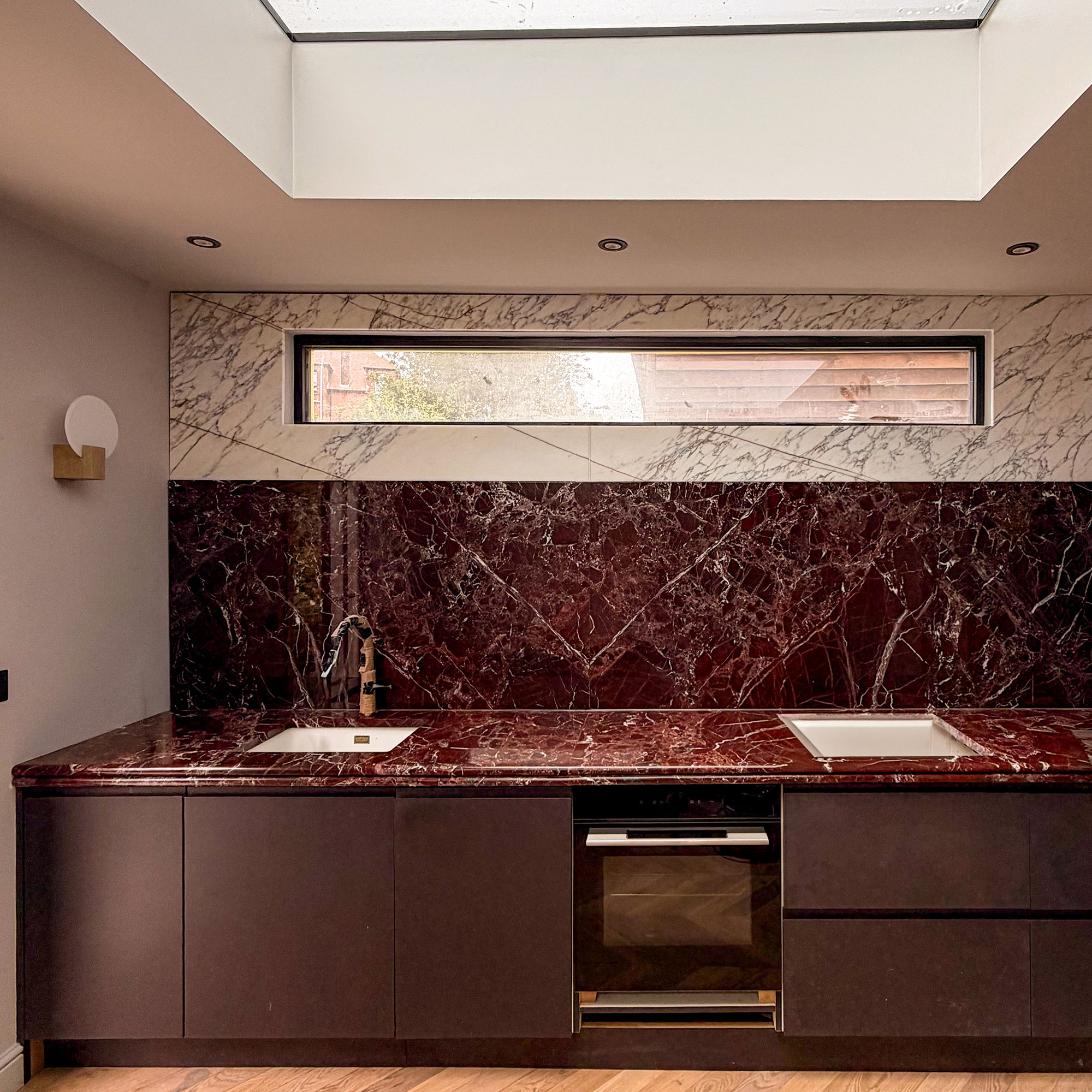 Kitchen with deep red cabinetry and deep red marble worktops and splashback below white marble wall
