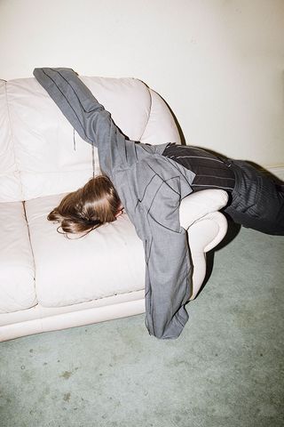 faceless model slouched over with face on couch wearing suit trousers on arms