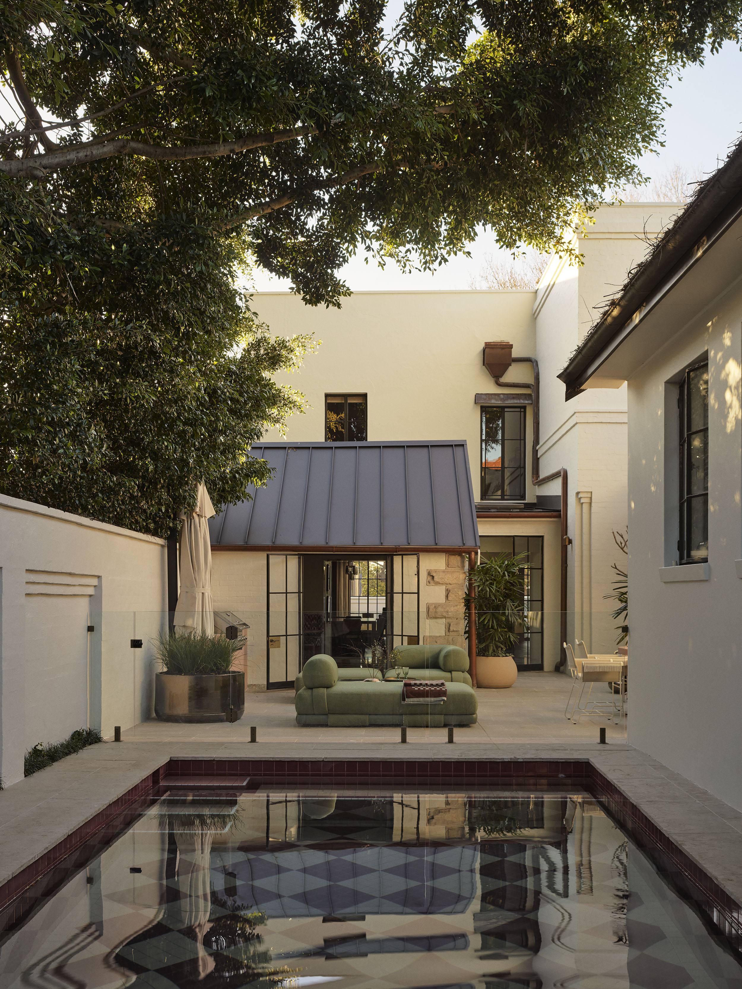 Rear garden of Smac Studio's renovated Art Deco home, featuring a pink checkerboard pool, lush mature trees and contemporary outdoor living spaces that seamlessly connect with the house.