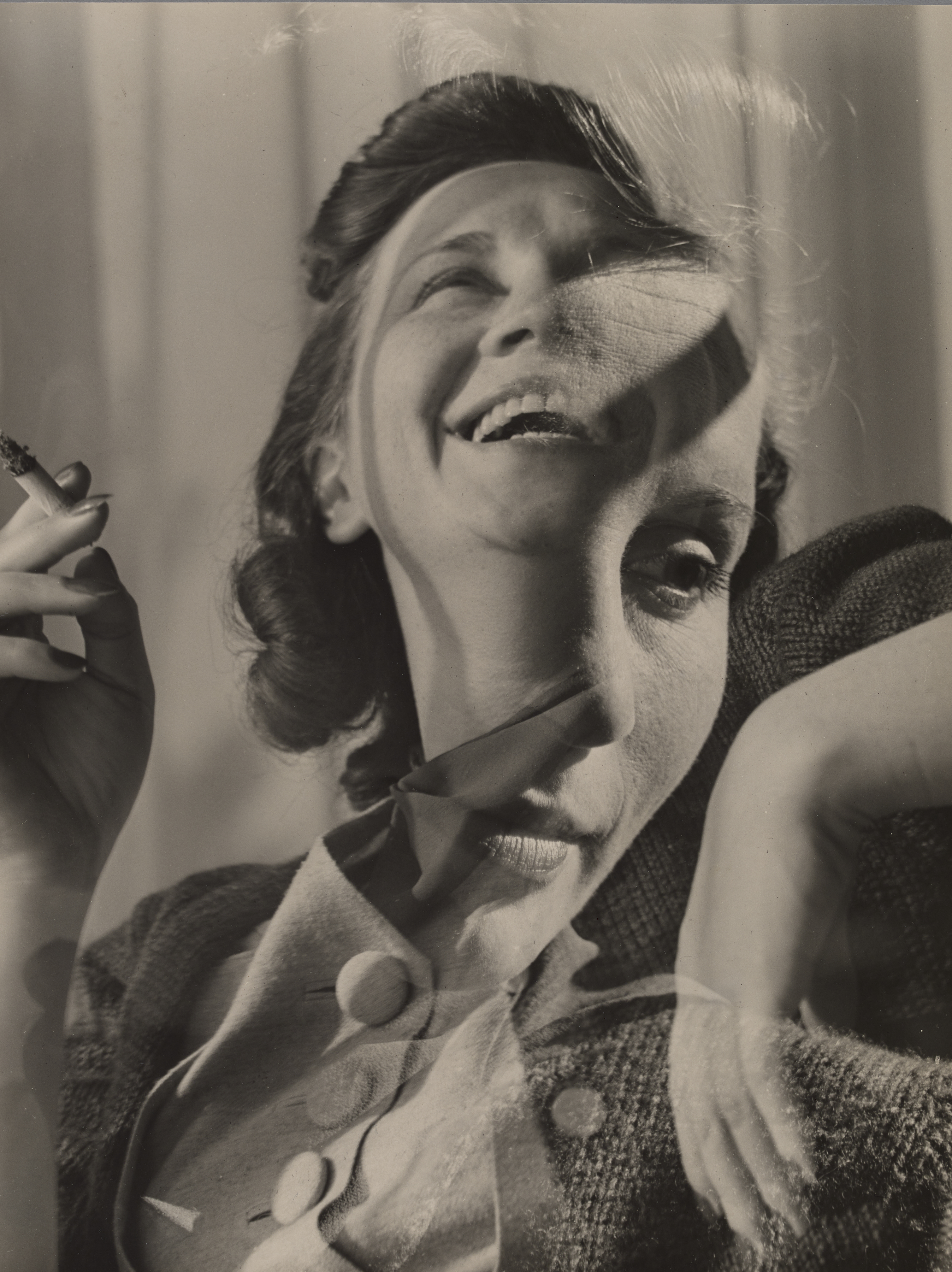 A double-exposed portrait of a laughing woman holding a cigarette, her face and shoulders ghosted with a second overlapping image of herself.